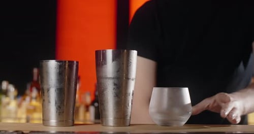 Bartender Puts Big Ice Cube to the Frozed Cocktail Glass By Forceps Making the Cocktail in the Bar