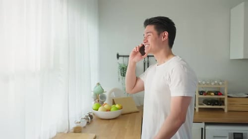 Asian handsome man talk on mobile phone call stand in kitchen at home.