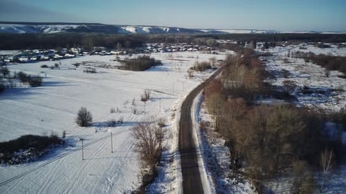 Aerial View of an Asphalt Road Surrounded By Snow in the Countryside