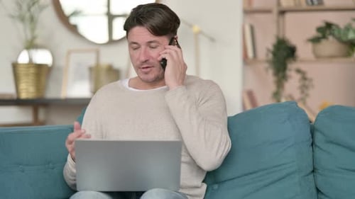 Man talking on phone while using laptop