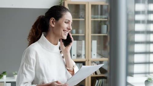 Woman Talks on Phone Holding Paper at Work