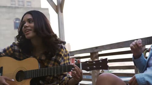 Young Women Sing and Play Guitar on Rooftop