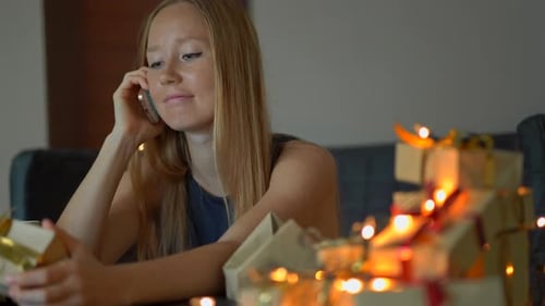 A Young Woman Pack Presents and Talk on a Cellphone. Present Wrapped in Craft Paper with a Red and
