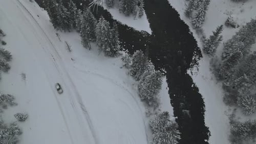 Aerial Top View of Forest During Winter Snowfall with Curved River