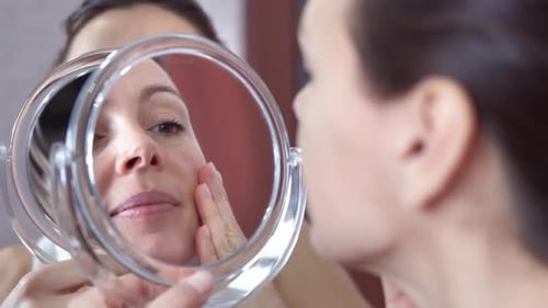 Woman Examining Face in Mirror Close Up