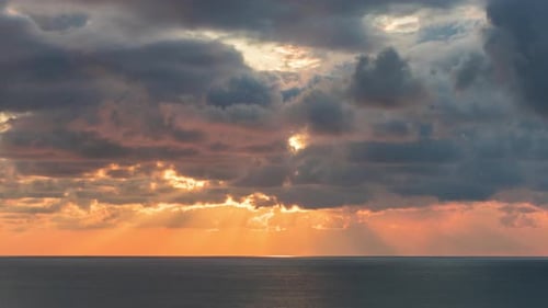 Clouds Crossing the Sky Over the Sea Horizon at Sunset with Sun Rays Emerge Through the Storm Clouds