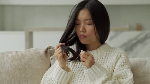 Asian Woman Sitting on the Couch with Hair Problems Brittle Damaged Dry Dirty and Falling Out Hair