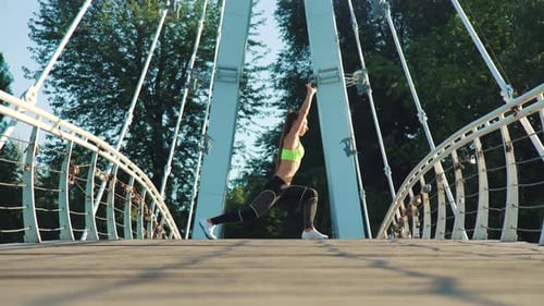 Active woman exercising and stretching in city park on footbridge.