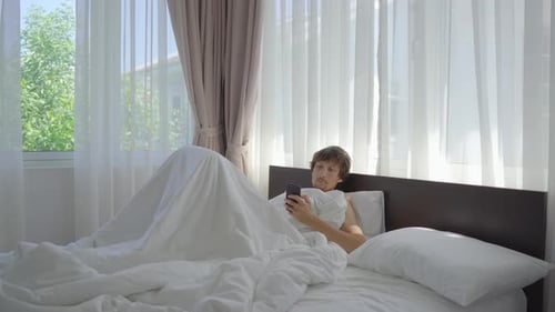Man Lies in Bed Using Smartphone