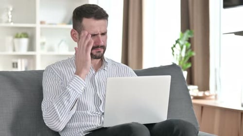 Man with Headache Using Laptop on Couch
