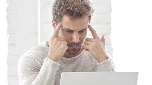 Man with Headache Massaging Temples at Desk
