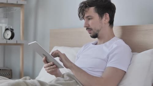 Young Adult Relaxing in Bed with Tablet
