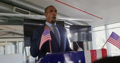 Man Giving Speech at Podium with American Flags