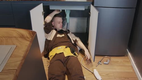 Plumber Repairing Sink Under Kitchen Cabinet