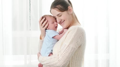 Mother Holds Newborn Baby in Window Light