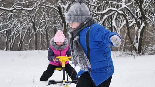 Petit garçon chevauche une fille sur un traîneau en hiver dans une forêt enneigée