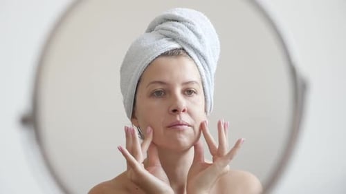 Woman Applying Lotion To Face With Towel On Head