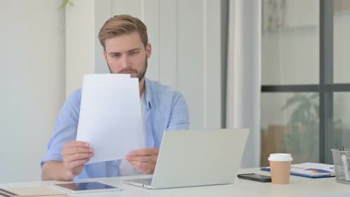Creative Man with Laptop Reading Documents in Office