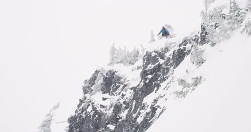 Snowboarder landet gefährlichen Big Air Trick vom großen Felsen und reitet durch Winterpulverschnee