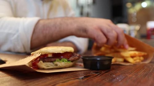Person Eating Burger and Dipping Fries in Sauce
