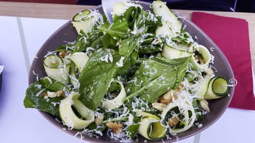 Preparing Fresh Salad With Greens, Zucchini, and Cheese