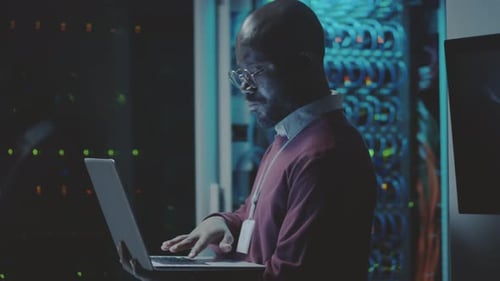 Man Uses Laptop in Dark Server Room