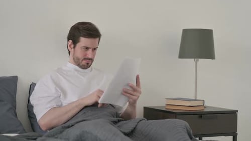 Man Sitting in Bed Reading Papers