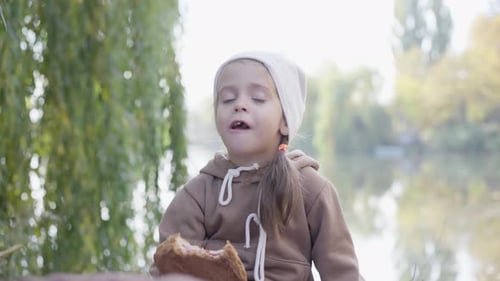 Little Girl Eating Bread by Lakeside