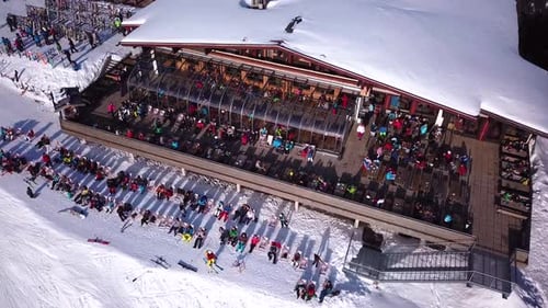 Aerial drone video of crowded ski restaurant with terrace full of people. Apres ski bar surrounded b