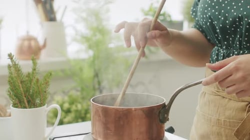 Woman Stirs Pot With Steam in Kitchen