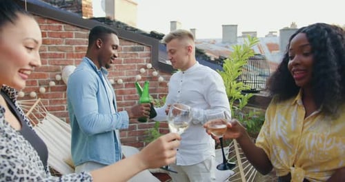 Des amis s'amusant ensemble sur le balcon, buvant de la bière et du vin et souriant beaucoup pendant une fête d'été