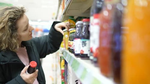 Woman In Supermarket Choosing Juice In Bottle