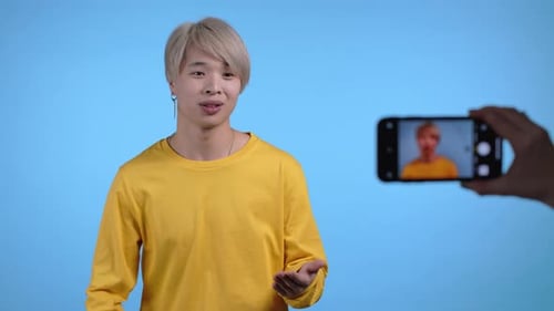 Lächelnder koreanischer Blogger-Mann macht mit seinem Smartphone auf Blau einen neuen Online-Videoblog-Vlog