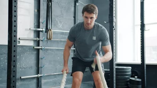Slow Motion of Young Man Working Out Battling Ropes Doing Crossfit Exercise in Gym