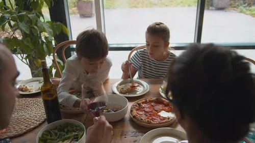 Boy Puts Fork in a Plate with Food, Girl Eats Pizza, Father Drinks Wine in a Cafe