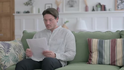Man Reads Documents on Couch Indoors