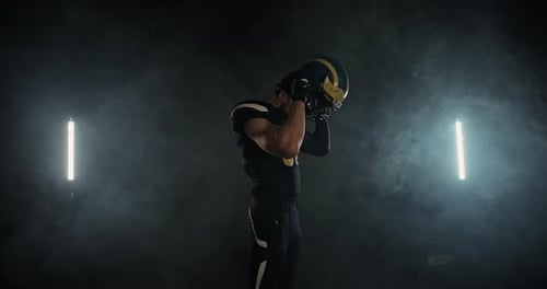 Football Player Putting On Helmet in Smoky Environment