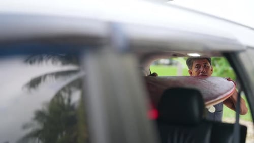 4K Asian senior man taking off surfboard from car trunk at the beach in sunny day