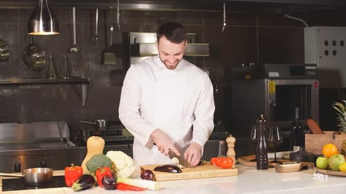 Junger Koch schneidet Auberginen auf einem Holzbrett im Inneren der Küche des modernen Restaurants