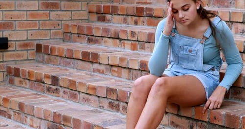 Sad schoolgirl sitting alone on staircase