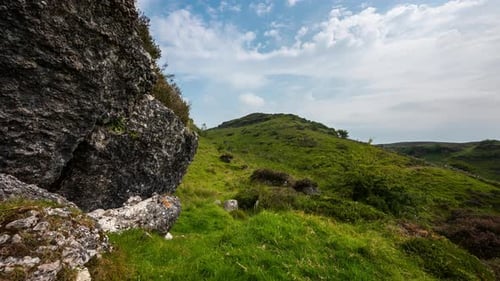 Panorama motion time lapse of rural landscape with large rocks in grass field on hillside during a c