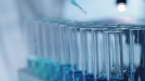 Nahaufnahme einer blauen Flüssigkeit, die aus der Pipette in das Teströhrchen tropft