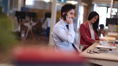 Young businessman talking on the phone with colleague in background