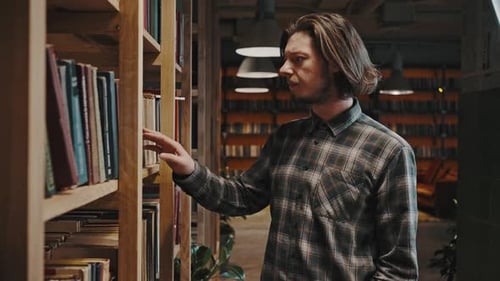 Jovem estudante sério andando pela biblioteca e pesquisando livros lendo rastreando tiro livre