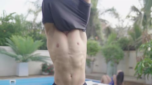 Handsome male take off shirt and walks towards girlfriend sitting by pool