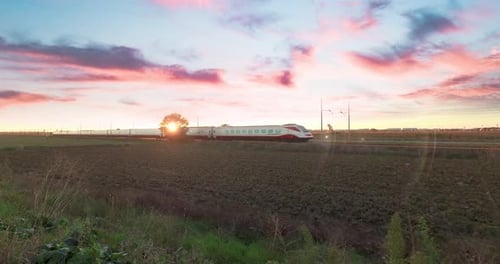 Der weiße und rote Hochgeschwindigkeitszug fährt gegen einen wunderschönen Himmel bei Sonnenuntergang