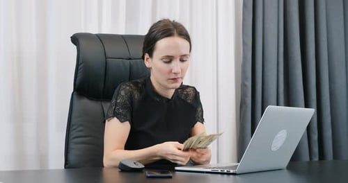 Young confident woman counting american dollar bills in office