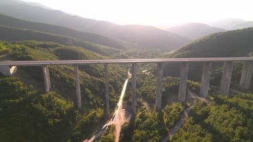 Aerial Side View of Long Viaduct Highway Between Green Hills at Sunset