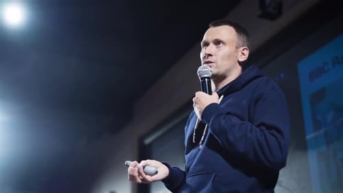 Um palestrante jovem e carismático com microfone fala ao público sobre as inovações de TI