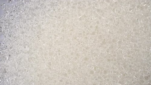 Zuckerkristalle fallen auf Glas auf einem strahlend weißen Hintergrund